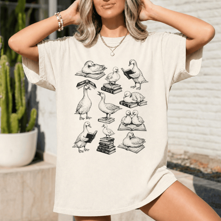 A woman wearing a white t-shirt with a graphic design of ducks reading books.