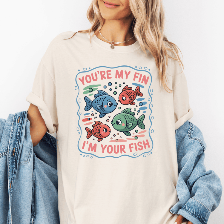A woman wearing a white t-shirt with a graphic design featuring colorful fish and the text "You're my fin, I'm your fish" printed on it.