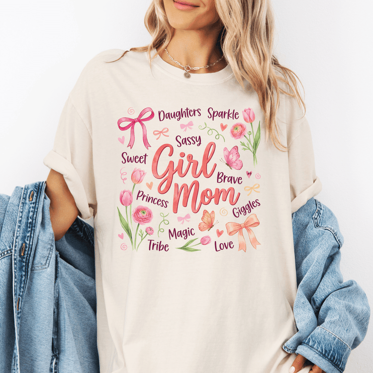 A woman wearing a white t-shirt with a graphic design featuring various words and illustrations related to a mother, such as "Daughters Sparkle", "Sweet Girl", "Giggles", "Tribe", and "Love".