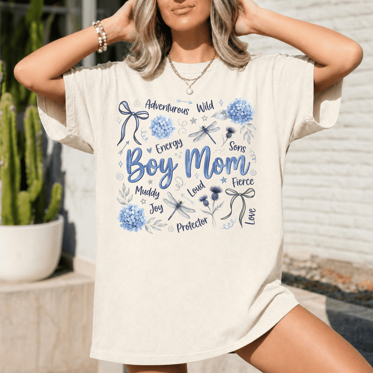 A woman wearing a white t-shirt with a graphic design featuring various words and illustrations related to a boy's mother.