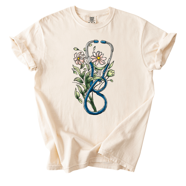A white t-shirt with a graphic design depicting a stethoscope surrounded by flowers and leaves.