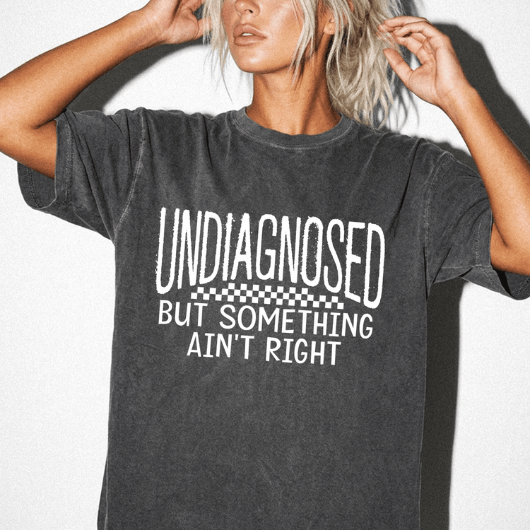 A woman wearing a black t-shirt with the text "UNDIAGNOSED BUT SOMETHING AIN'T RIGHT" printed on it.