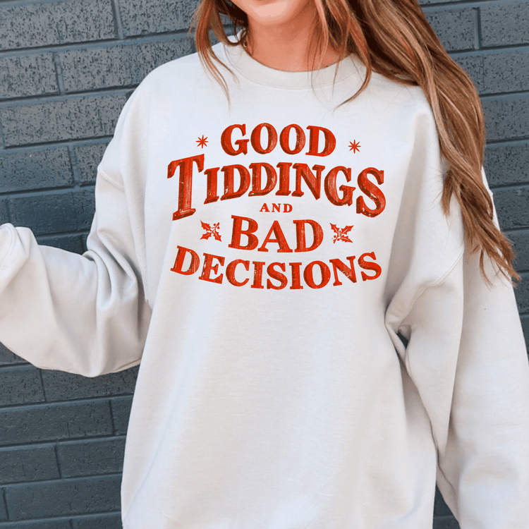 A person wearing a white sweatshirt with the text "GOOD TIDDINGS AND BAD DECISIONS" printed on it.