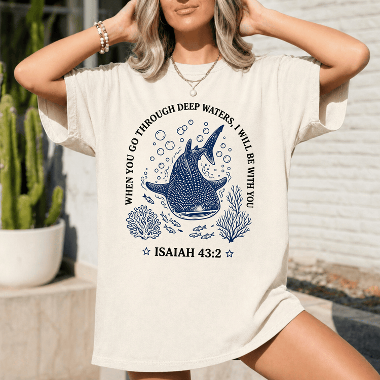 A woman wearing a white t-shirt with a graphic design featuring a blue whale surrounded by bubbles and marine life.
