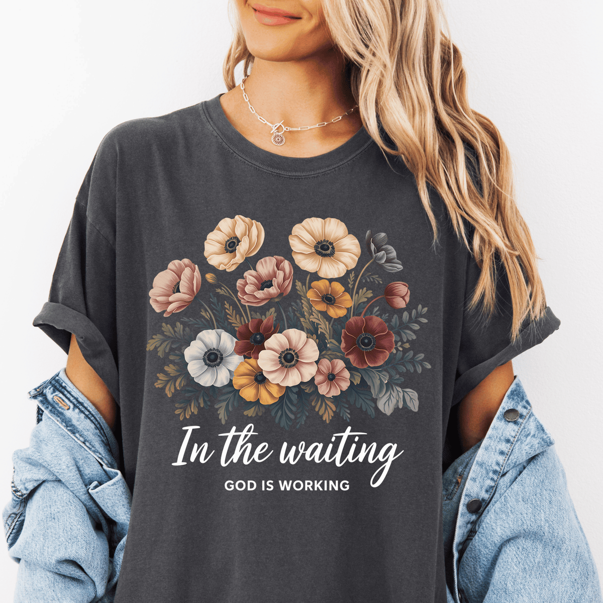 A woman wearing a gray t-shirt with a floral design and the text "In the waiting God is working" printed on it.