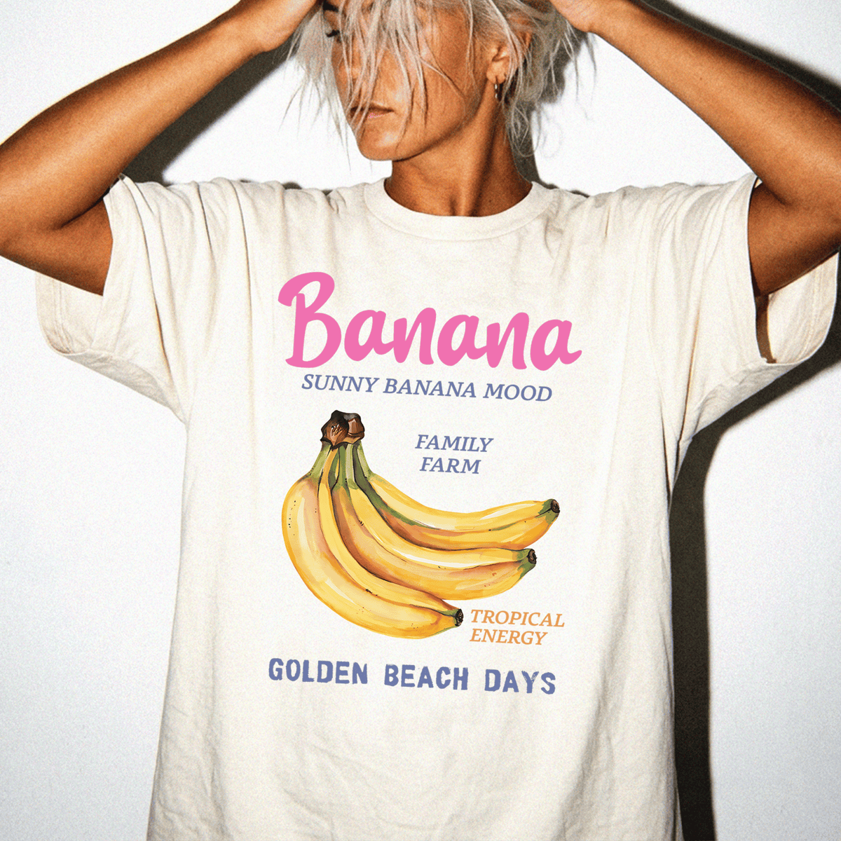 A person wearing a white t-shirt with a graphic of bananas and text that says "Banana SUNNY BANANA MIND FAMILY FARM TROPICAL ENERGY GOLDEN BEACH DAYS".