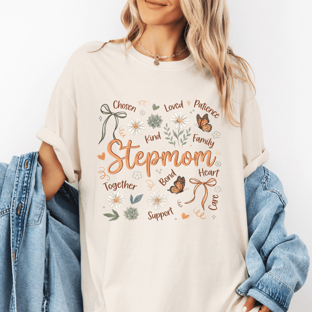 A woman wearing a white t-shirt with a graphic design featuring the word "Stepmom" surrounded by various words such as "Chosen", "Loved", "Patience", "Kind", "Family", "Support", "Together", and "Love".