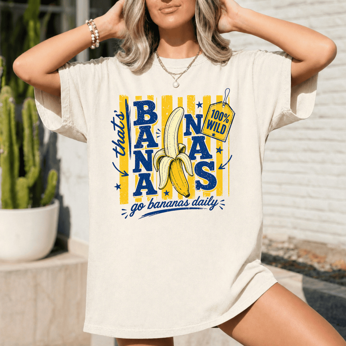 A woman wearing a white t-shirt with a graphic design featuring a banana and the text "That's 100% wild go bananas daily".