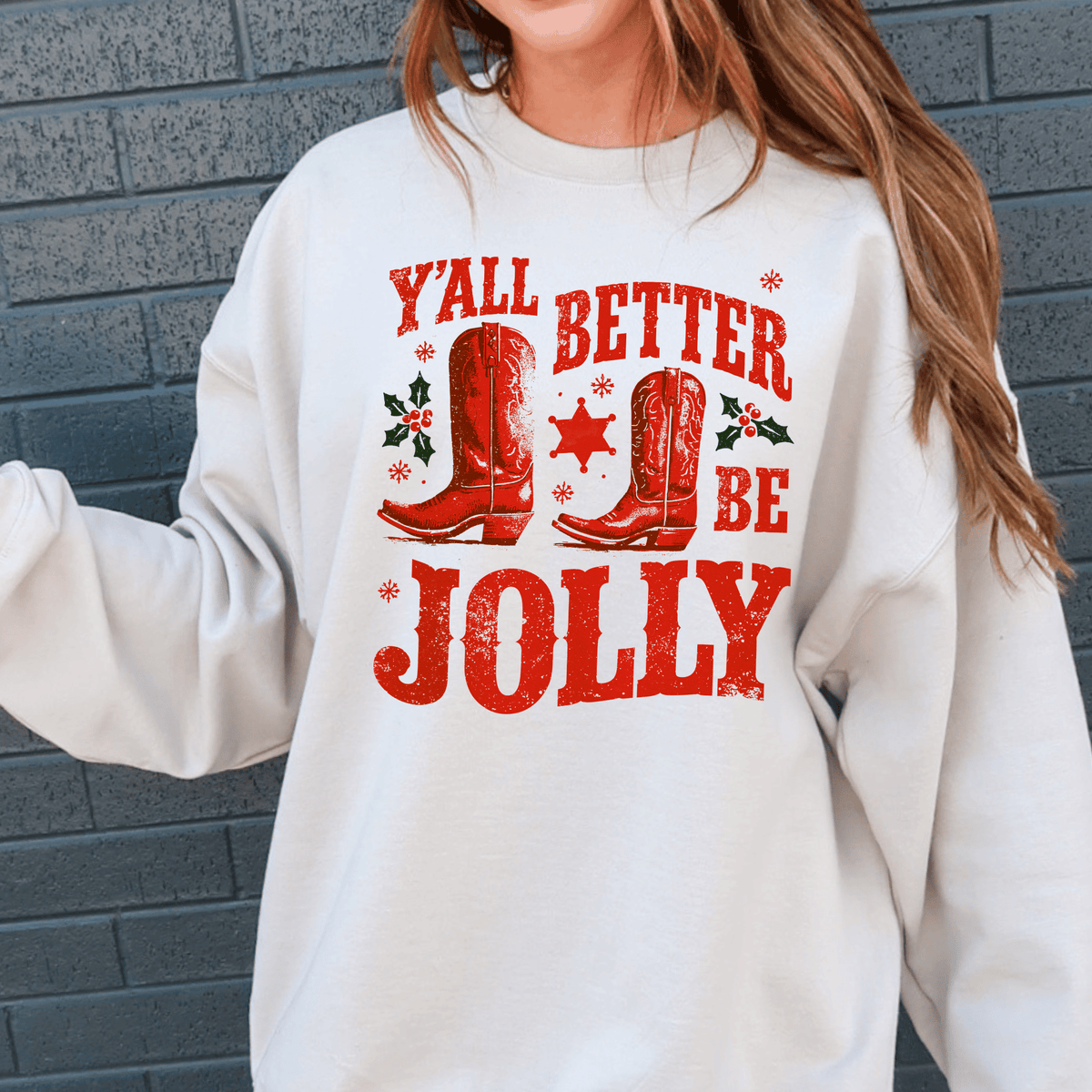 A white sweatshirt with a red and white graphic design featuring a pair of red cowboy boots and the text "Y'ALL BETTER BE JOLY" printed on it.
