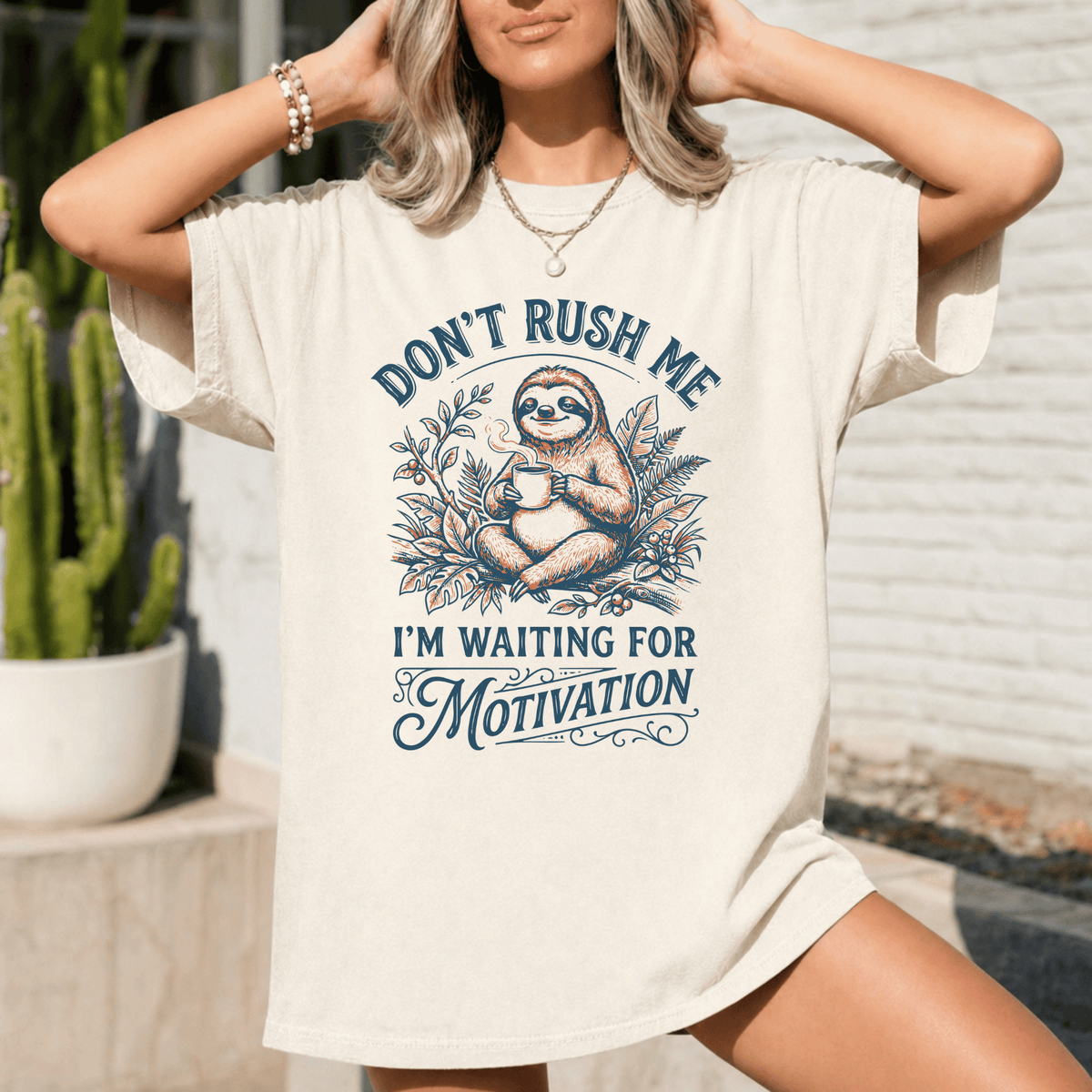 A woman wearing a white t-shirt with a graphic design of a sloth and the text "Don't Rush Me I'm Waiting for Motivation".