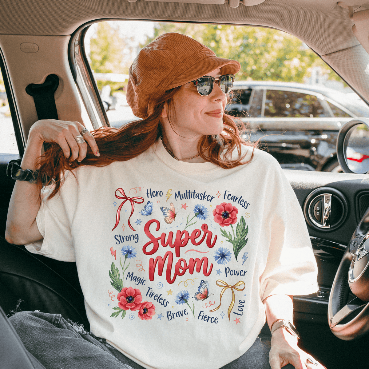 A woman wearing a white t-shirt with a colorful design and text, sitting in a car.