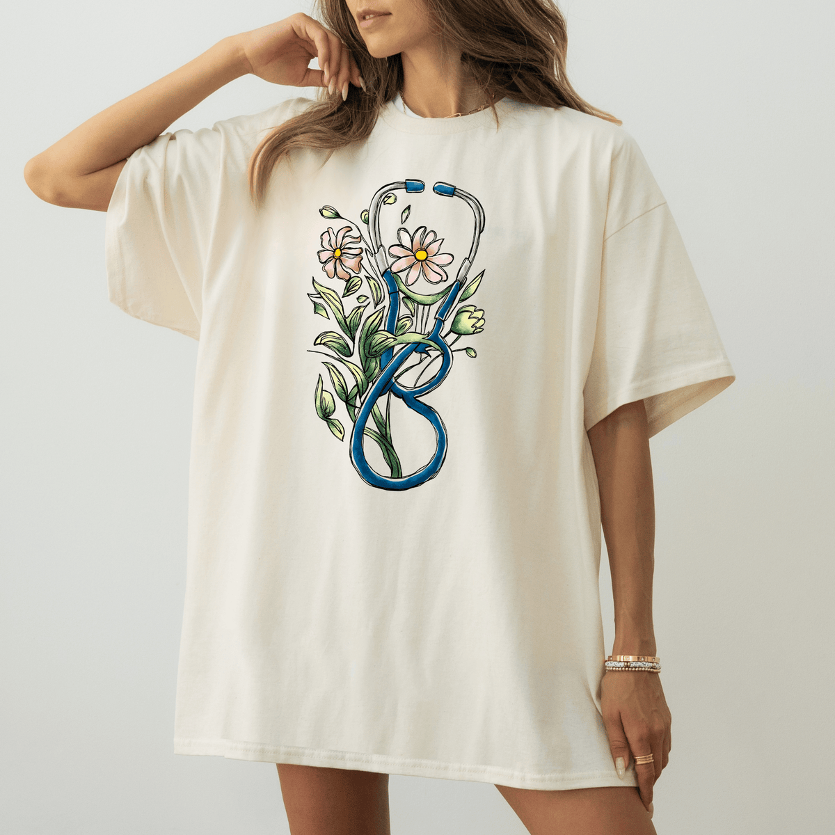 A woman wearing a white t-shirt with a colorful graphic design of a stethoscope surrounded by flowers.