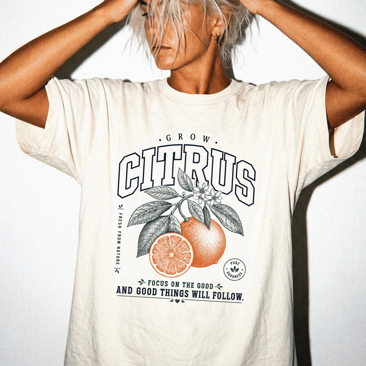 A person wearing a white t-shirt with a graphic design of an orange and leaves, along with the text "GROW CITRUS" and "FOCUS ON THE GOOD AND GOOD THINGS WILL FOLLOW".