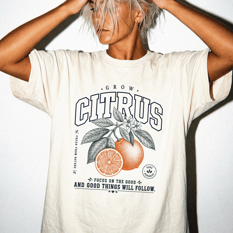 A person wearing a white t-shirt with a graphic design of an orange and leaves, along with the text "GROW CITRUS" and "FOCUS ON THE GOOD AND GOOD THINGS WILL FOLLOW".