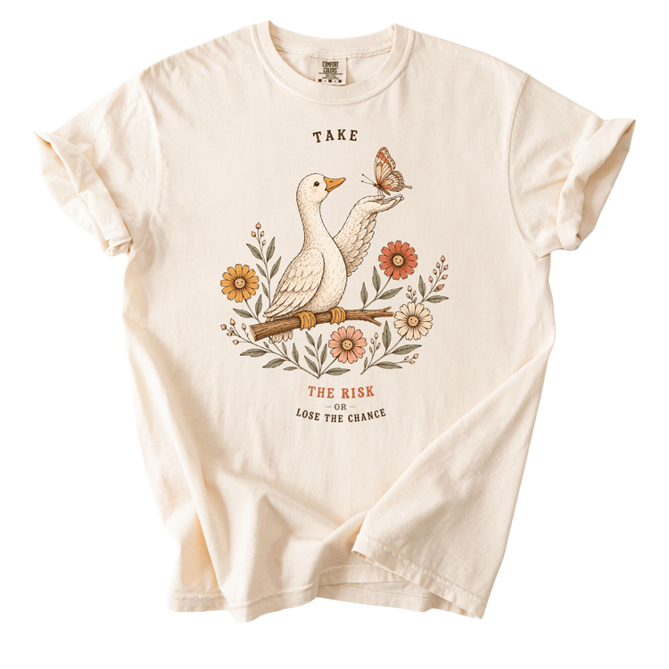 a white t-shirt with a graphic design depicting a bird holding a butterfly and flowers. The text on the t-shirt reads "TAKE THE RISK LOSE THE CHANCE".