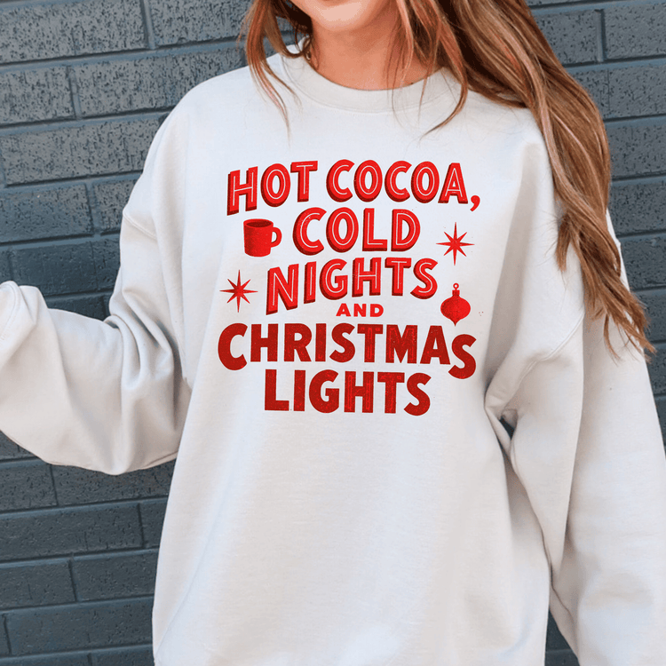 A white sweatshirt with red text that says "HOT COCOA, COLD NIGHTS AND CHRISTMAS LIGHTS".