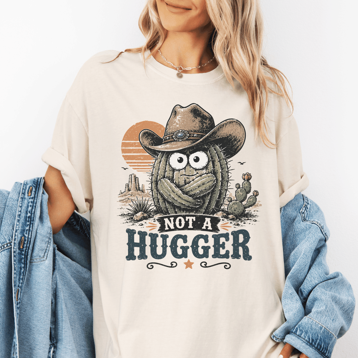 A woman wearing a white t-shirt with a graphic design of a cactus wearing a cowboy hat and the text "NOT A HUGGER" printed on it.