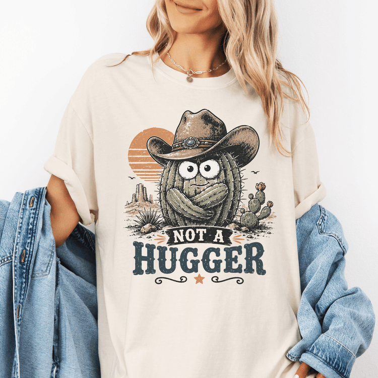 A woman wearing a white t-shirt with a graphic design of a cactus wearing a cowboy hat and the text "NOT A HUGGER" printed on it.
