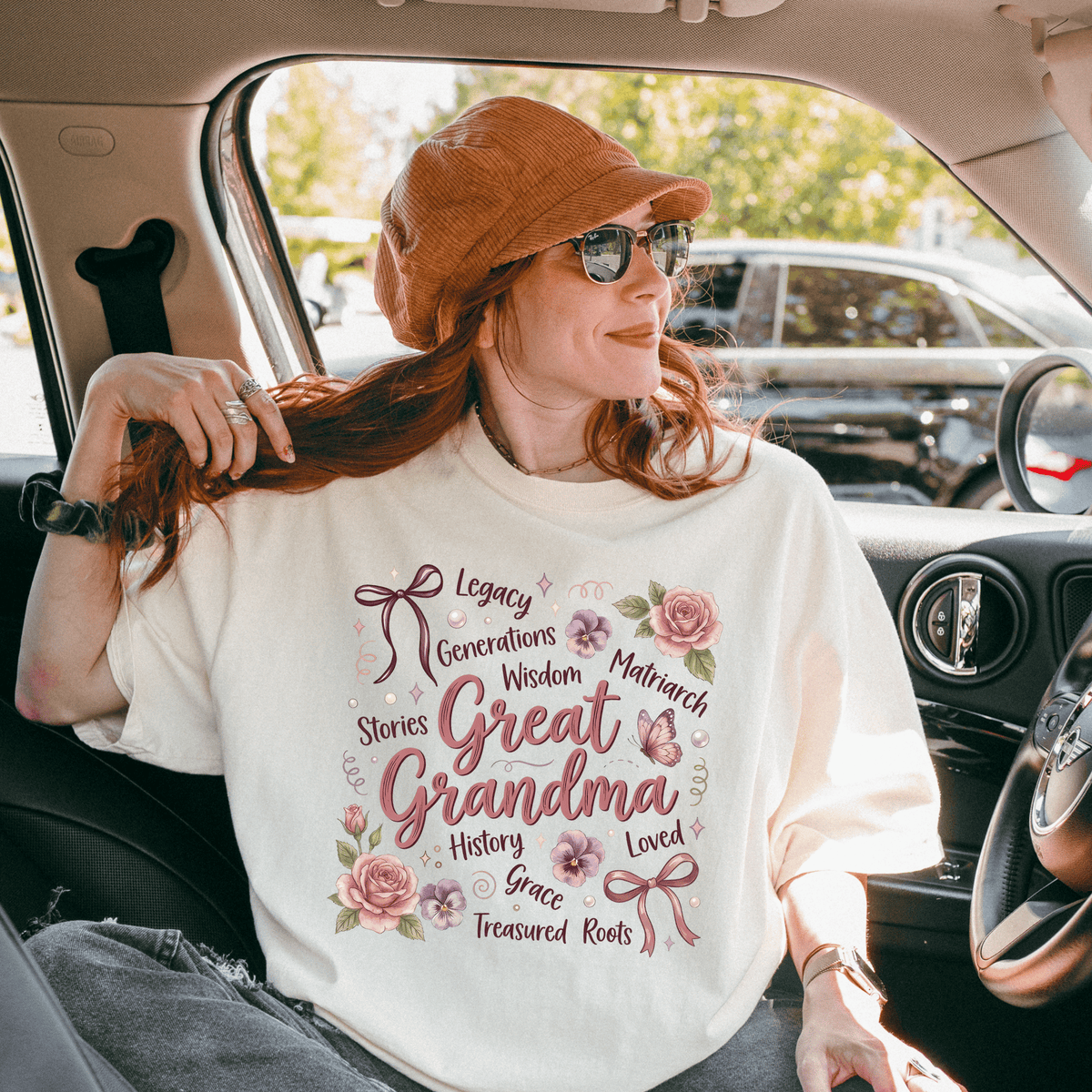 A woman wearing a white t-shirt with text and a bow on it, sitting in a car and smiling.