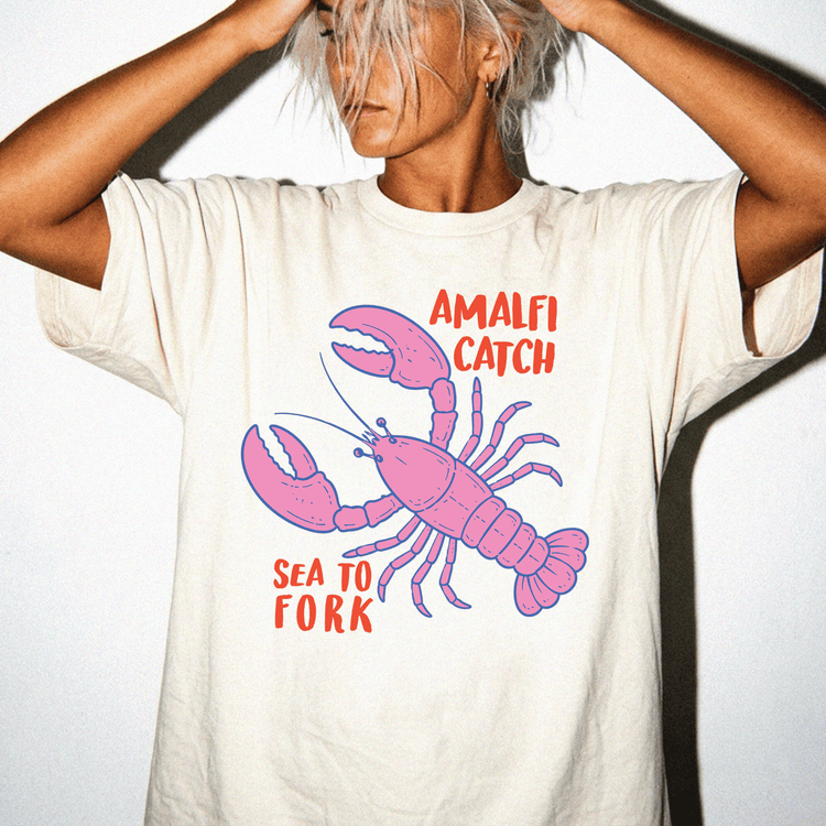 A person wearing a white t-shirt with a graphic of a lobster and the text "Amalfi Catch Sea to Fork" printed on it.