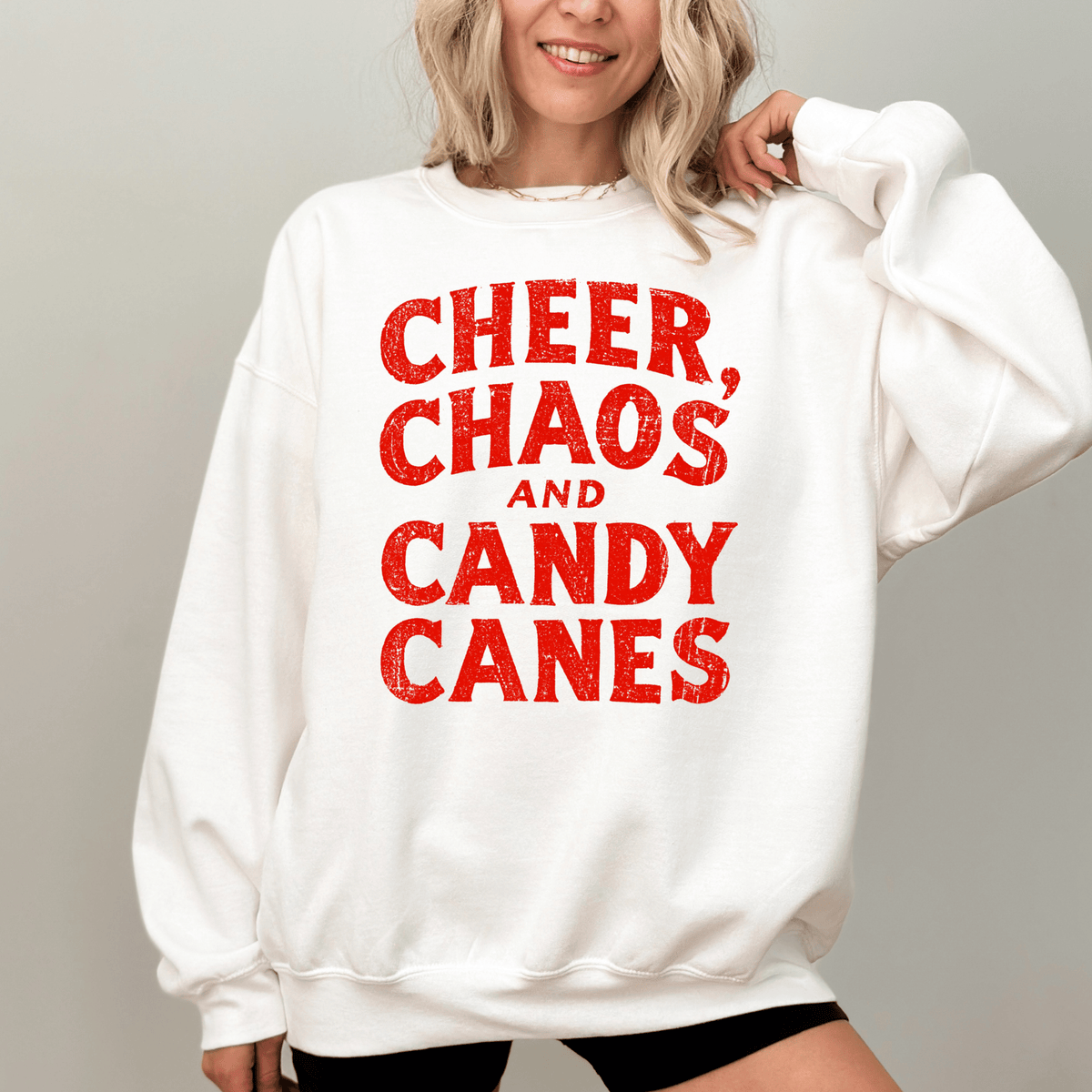 A woman wearing a white sweatshirt with the text "CHEER, CHAOS, AND CANDY CANES" printed on it.