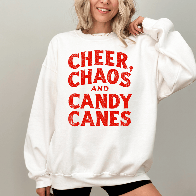 A woman wearing a white sweatshirt with the text "CHEER, CHAOS, AND CANDY CANES" printed on it.
