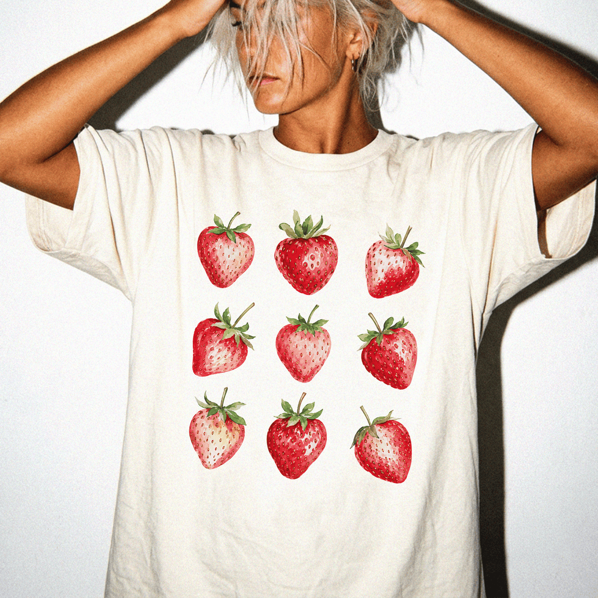 A person wearing a white t-shirt with a graphic of nine red strawberries on it.