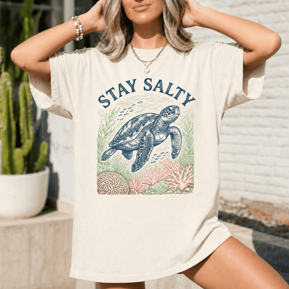 A woman wearing a white t-shirt with a graphic design of a sea turtle and coral, along with the text "STAY SALTY".