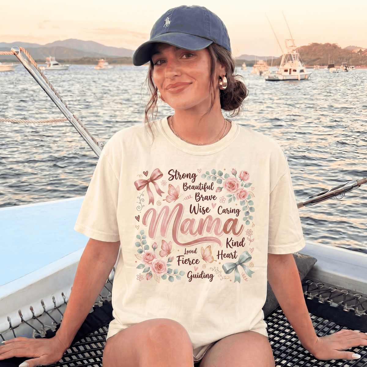 A woman wearing a white t-shirt with a floral design and text, sitting on a boat in the water with mountains in the background.