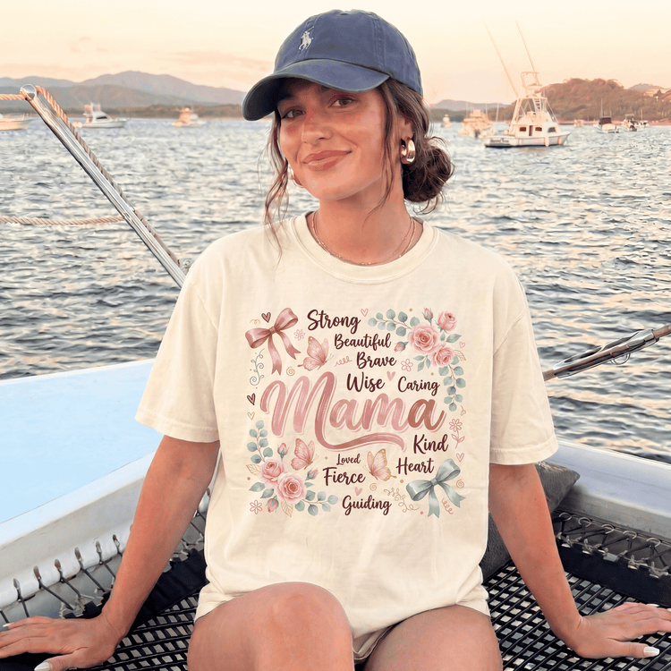 A woman wearing a white t-shirt with a floral design and text, sitting on a boat in the water with mountains in the background.
