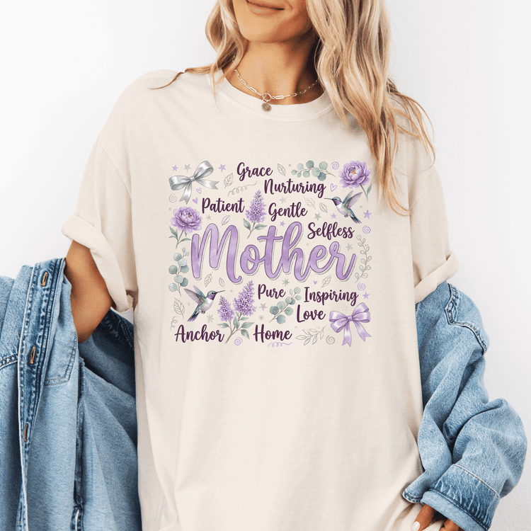 A woman wearing a white t-shirt with a graphic design featuring the word "Mother" surrounded by various floral and nature-inspired elements.
