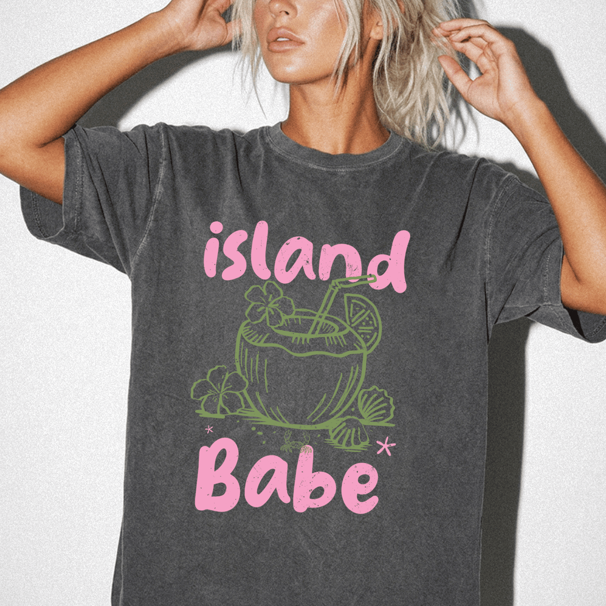 A woman wearing a gray t-shirt with a graphic design of a tropical drink and the text "island Babe" printed on it.
