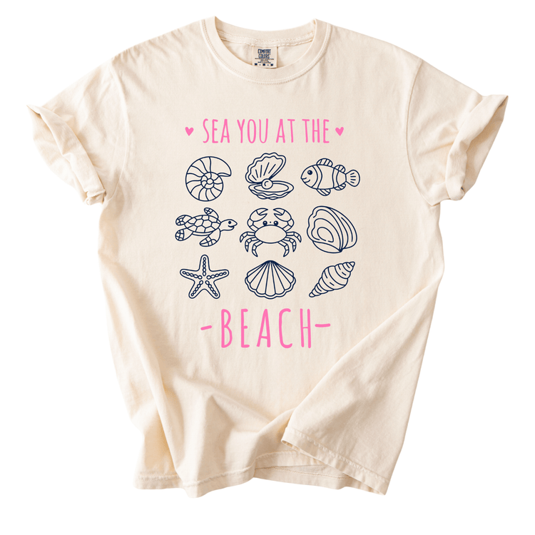 a white t-shirt with a graphic design of various sea creatures, including a crab, starfish, and seashells, along with the text "SEA YOU AT THE BEACH" printed on it.