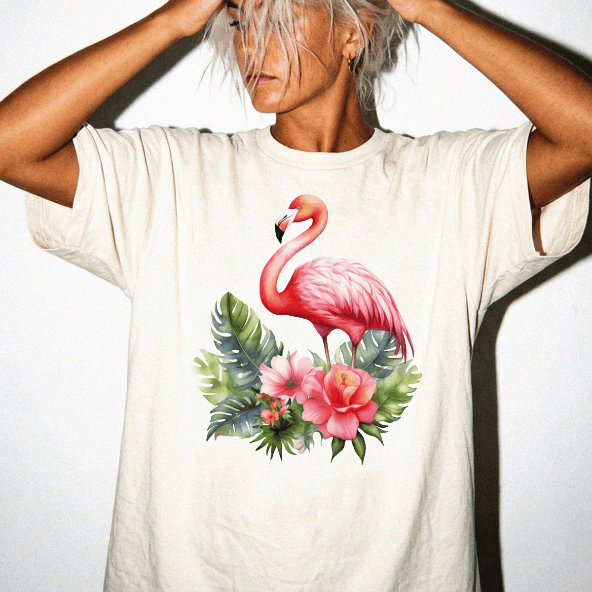 A person wearing a white t-shirt with a pink flamingo and tropical flowers printed on it.