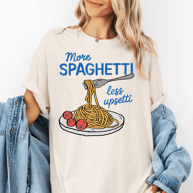 A woman wearing a white t-shirt with a graphic of spaghetti and a fork, along with the text "More spaghetti less upsti" printed on it.