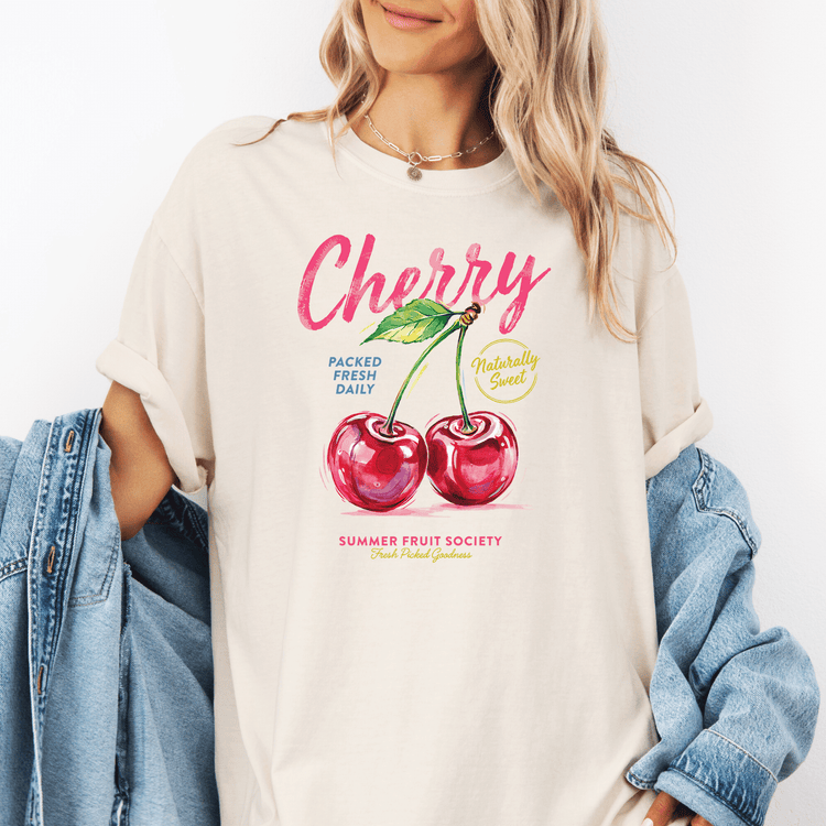 A woman wearing a white t-shirt with a graphic design of two cherries and text that says "cherry" and "packed fresh daily".