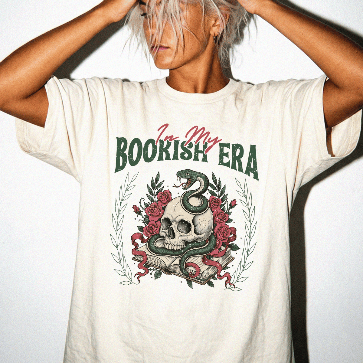 A person wearing a white t-shirt with a graphic design featuring a skull, a snake, and a book.