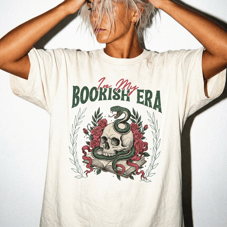 A person wearing a white t-shirt with a graphic design featuring a skull, a snake, and a book.