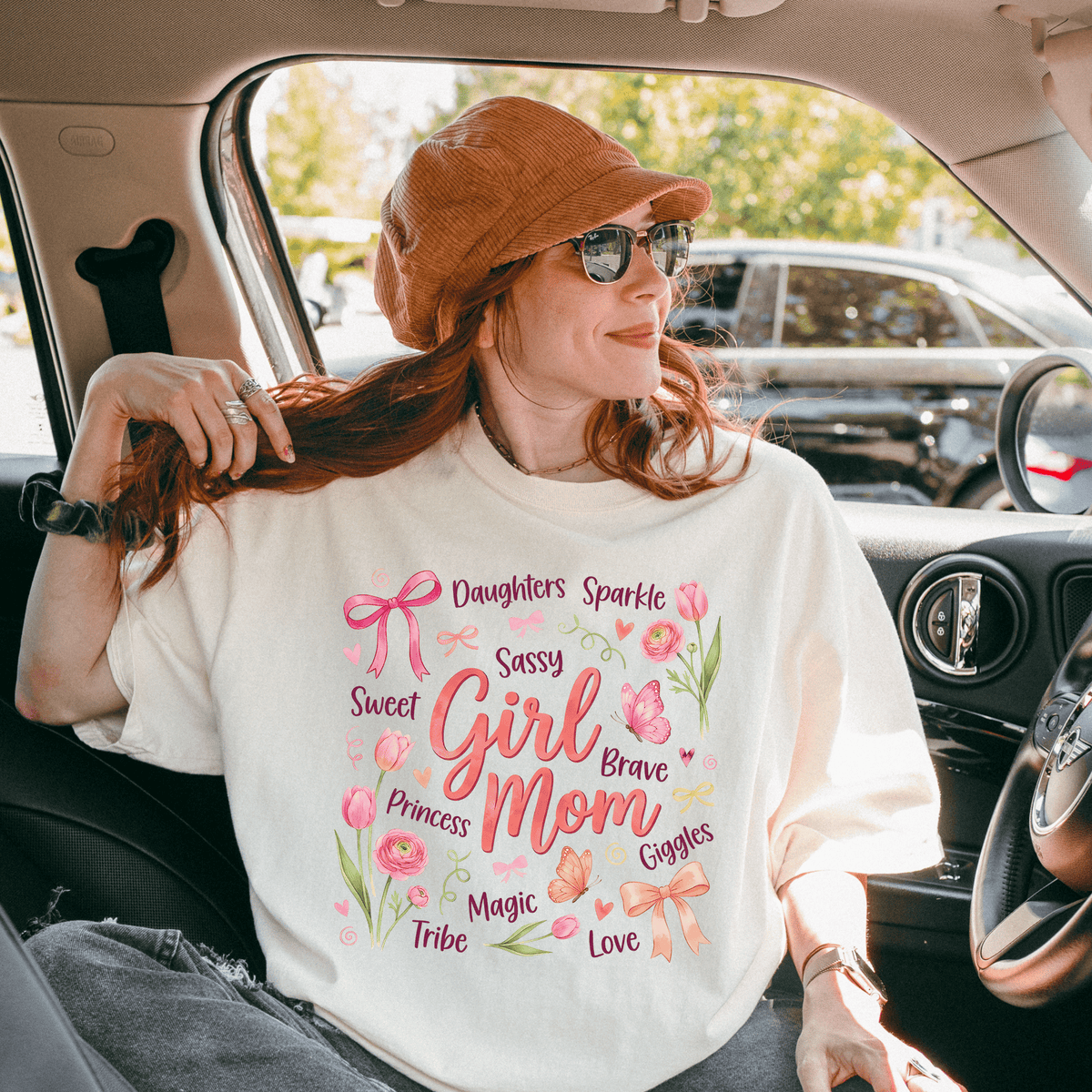 A woman wearing a white t-shirt with text and illustrations related to a girl's mom, sitting in a car.