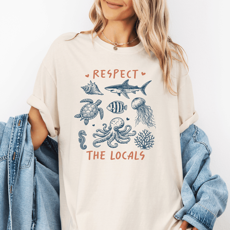 A woman wearing a white t-shirt with a graphic design of marine life and the text "RESPECT THE LOCALS" printed on it.
