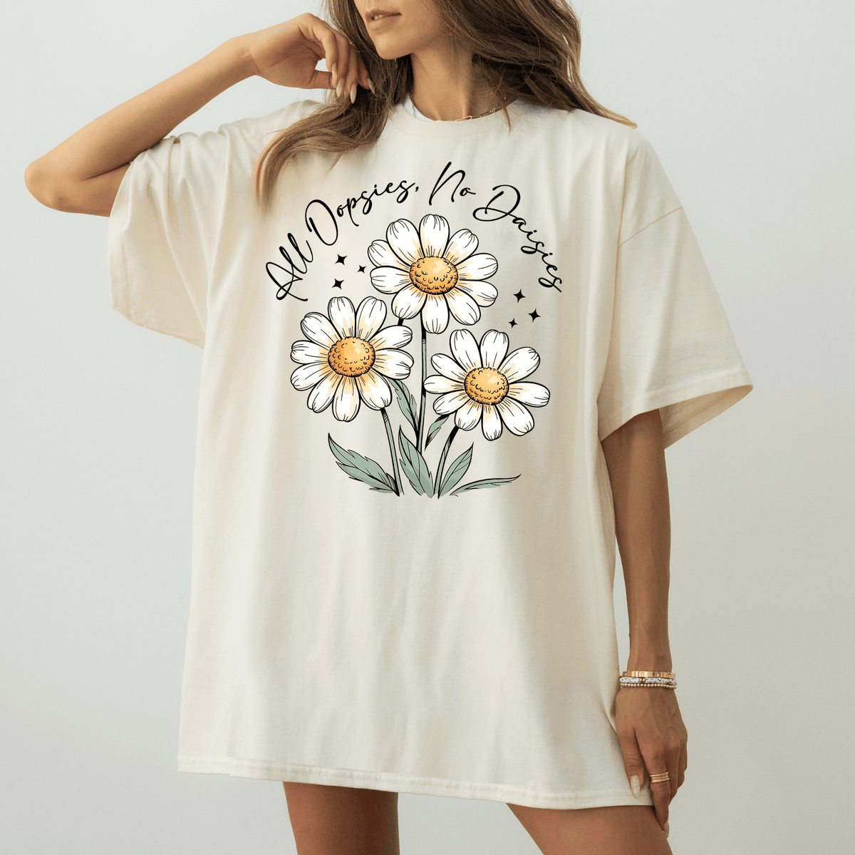 A woman wearing a white t-shirt with a graphic design of three white daisies and the text "All Dopsies No Dopsies" printed on it.