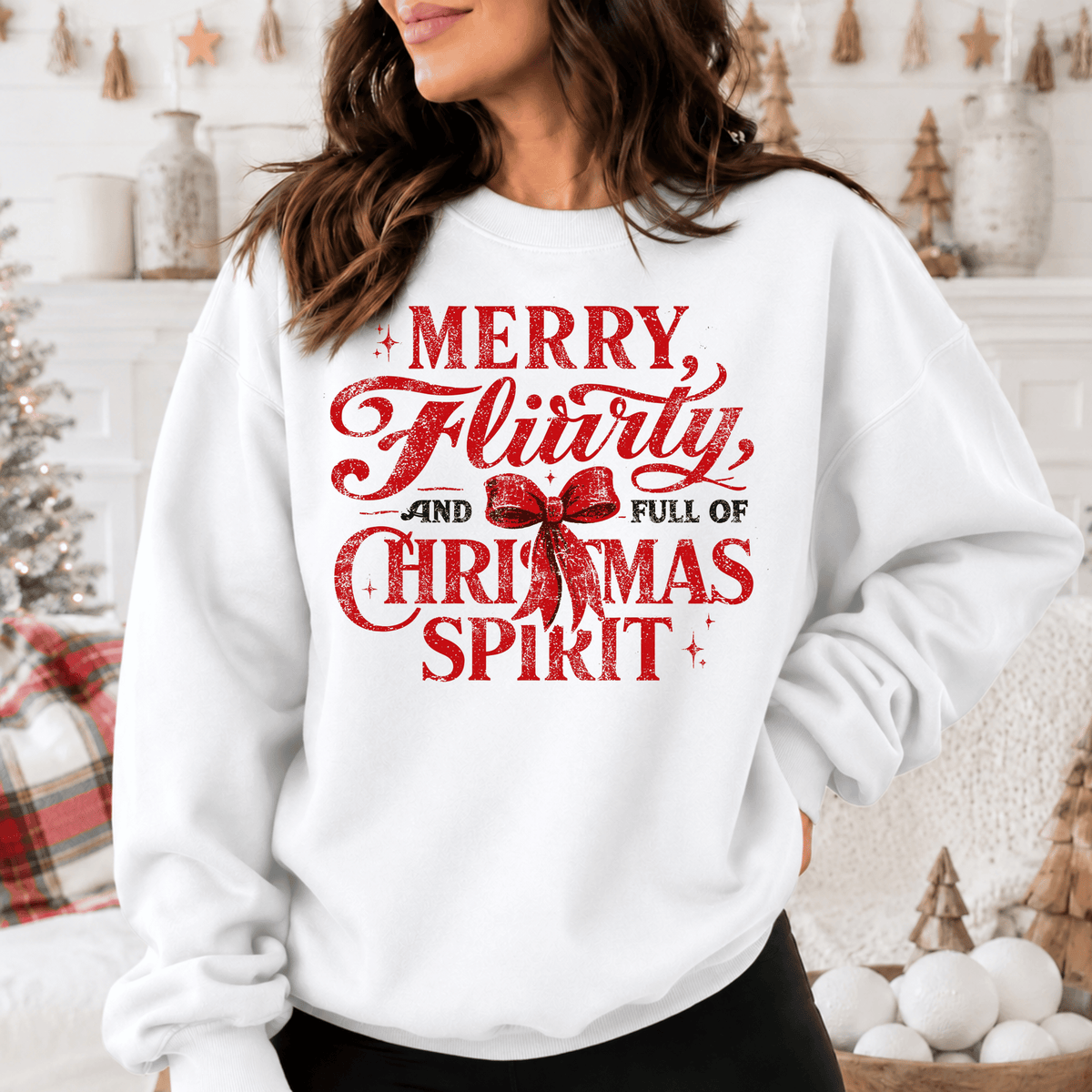 A woman wearing a white sweatshirt with a red and white text design that says "MERRY FLIRTY AND FULL OF CHRISTMAS SPIRIT".