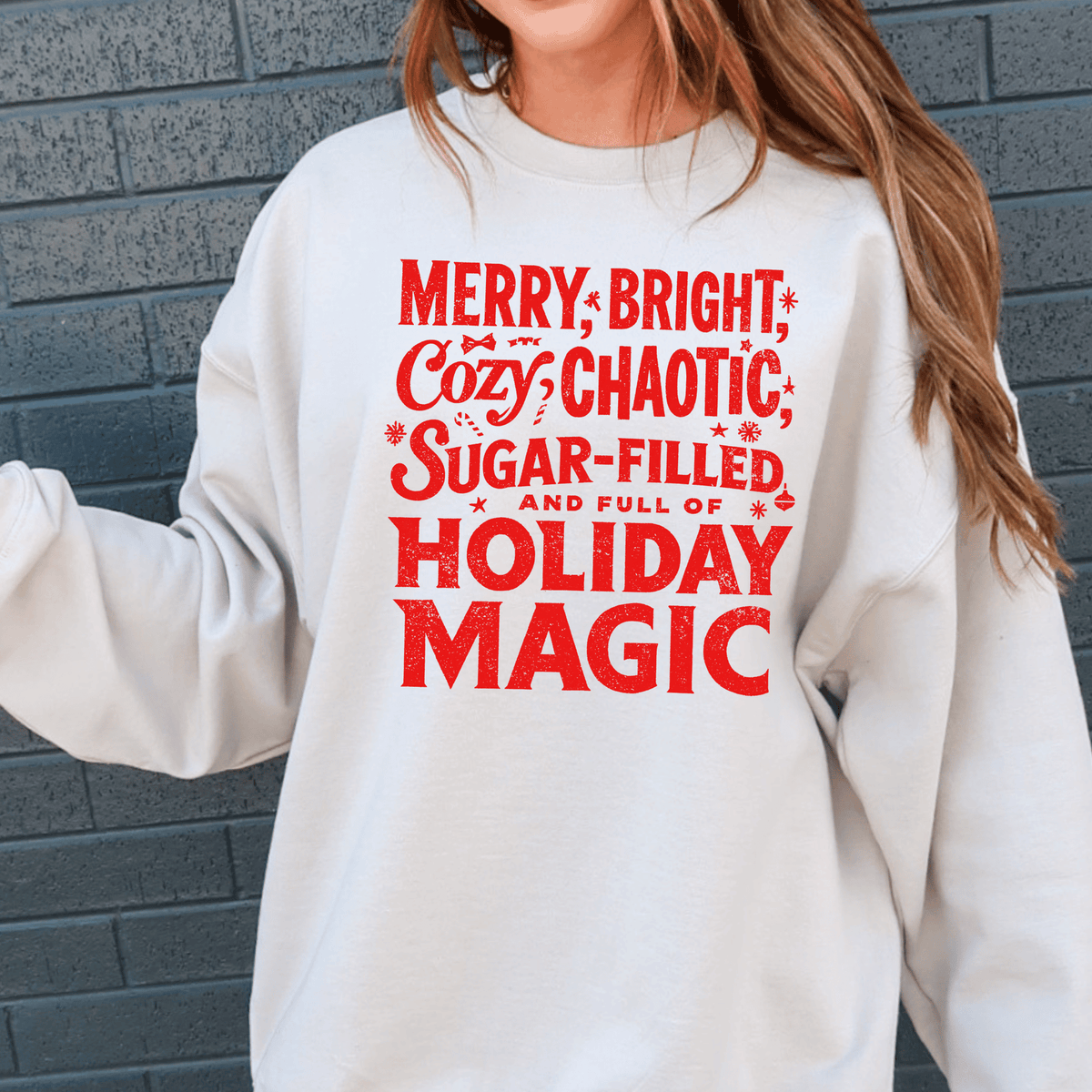 A white sweatshirt with red text that reads "MERRY, BRIGHT, COZY, CHAOTIC, SUGAR-FILLED AND FULL OF HOLIDAY MAGIC".