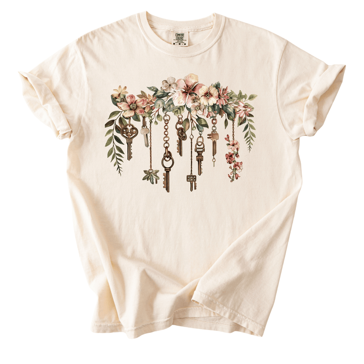 A white t-shirt with a floral design featuring a row of keys hanging from a branch.