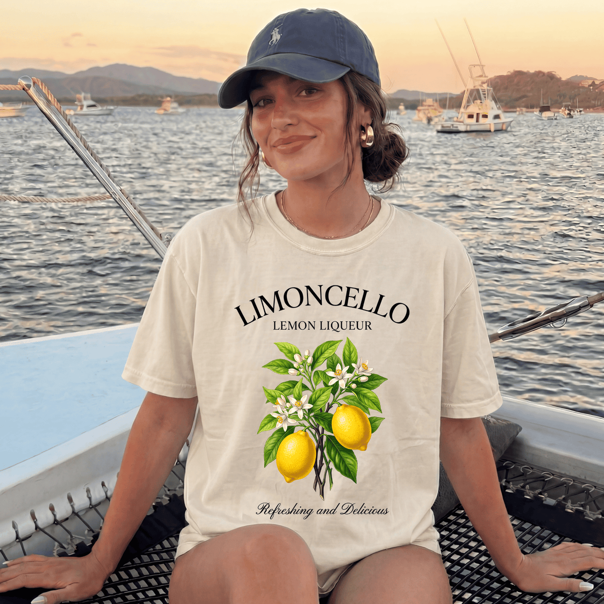 A woman wearing a cap and a white t-shirt with a lemon graphic is sitting on a boat, smiling at the camera.