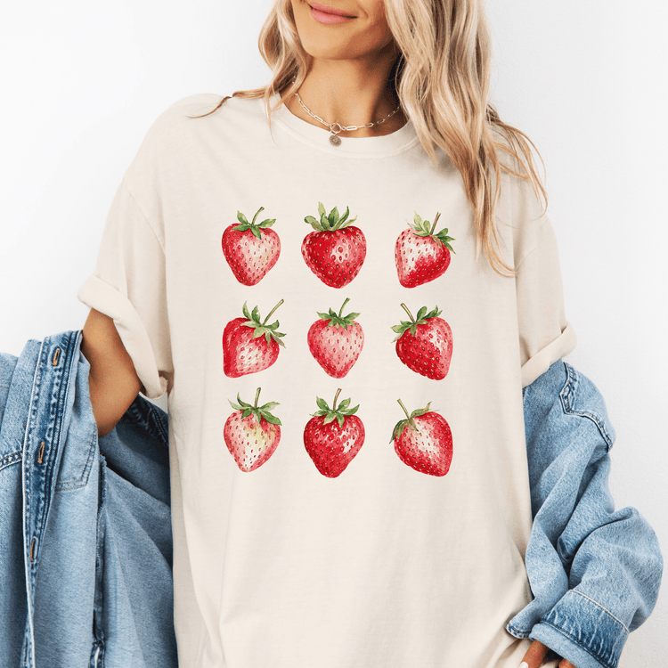 A woman wearing a white t-shirt with a graphic of nine red strawberries printed on it.