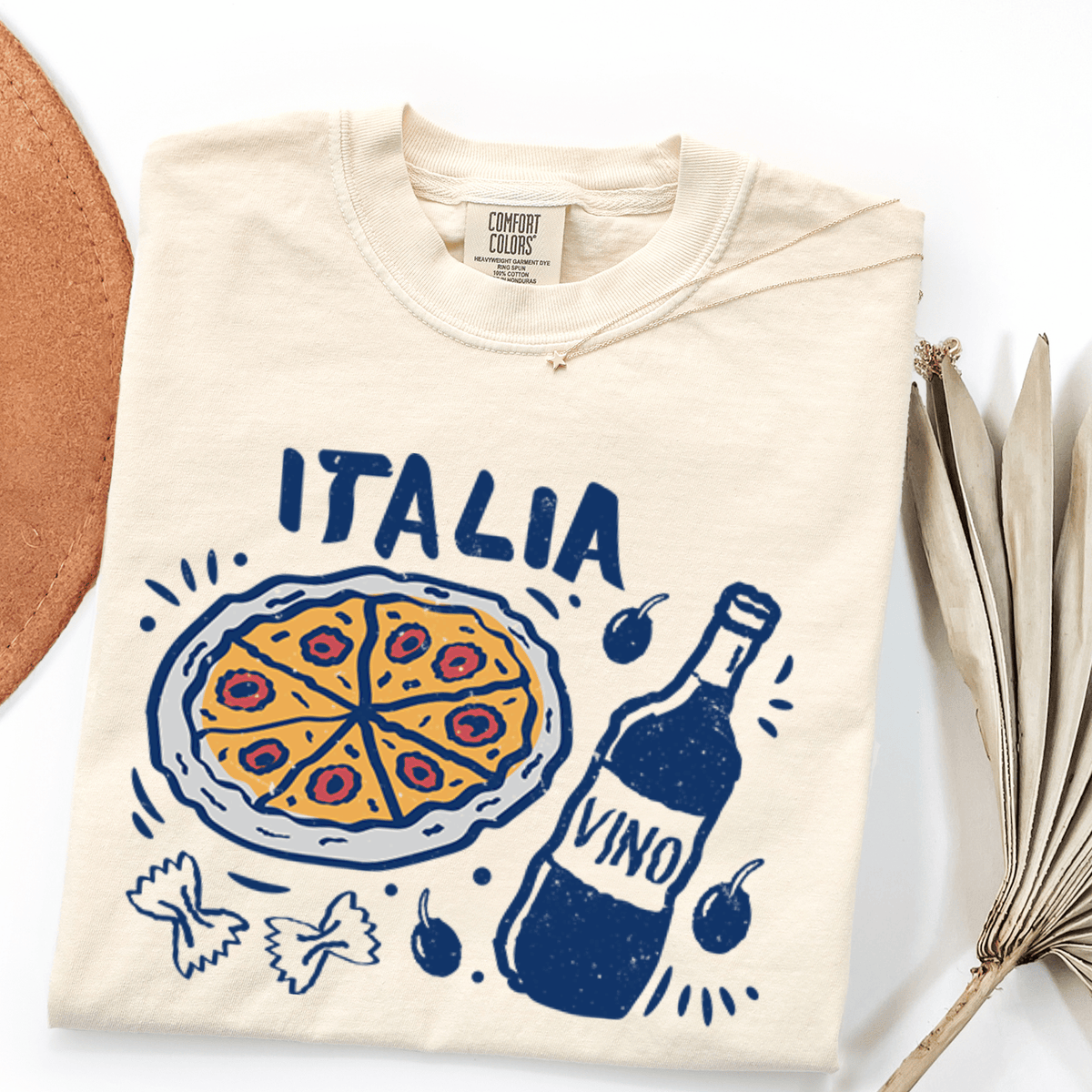 a white t-shirt with a graphic design depicting a pizza, a bottle of wine, and various Italian food items such as olives and pasta.