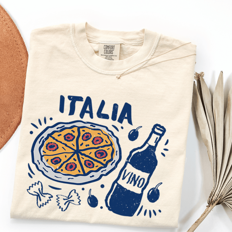 a white t-shirt with a graphic design depicting a pizza, a bottle of wine, and various Italian food items such as olives and pasta.
