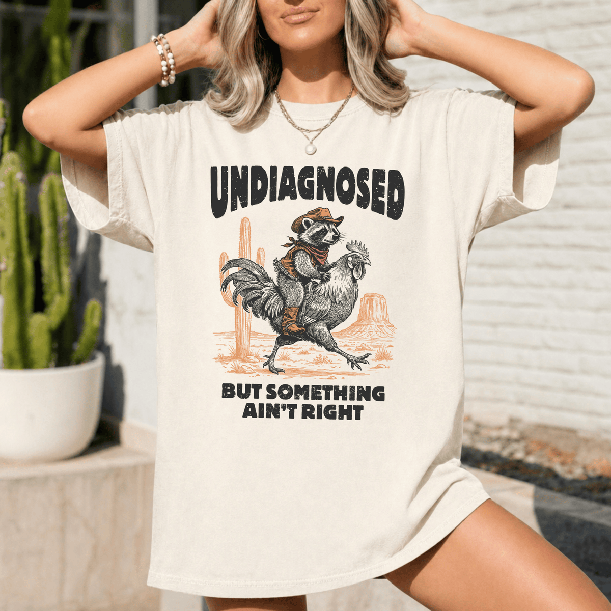 A woman wearing a white t-shirt with a graphic design featuring a raccoon riding a rooster.