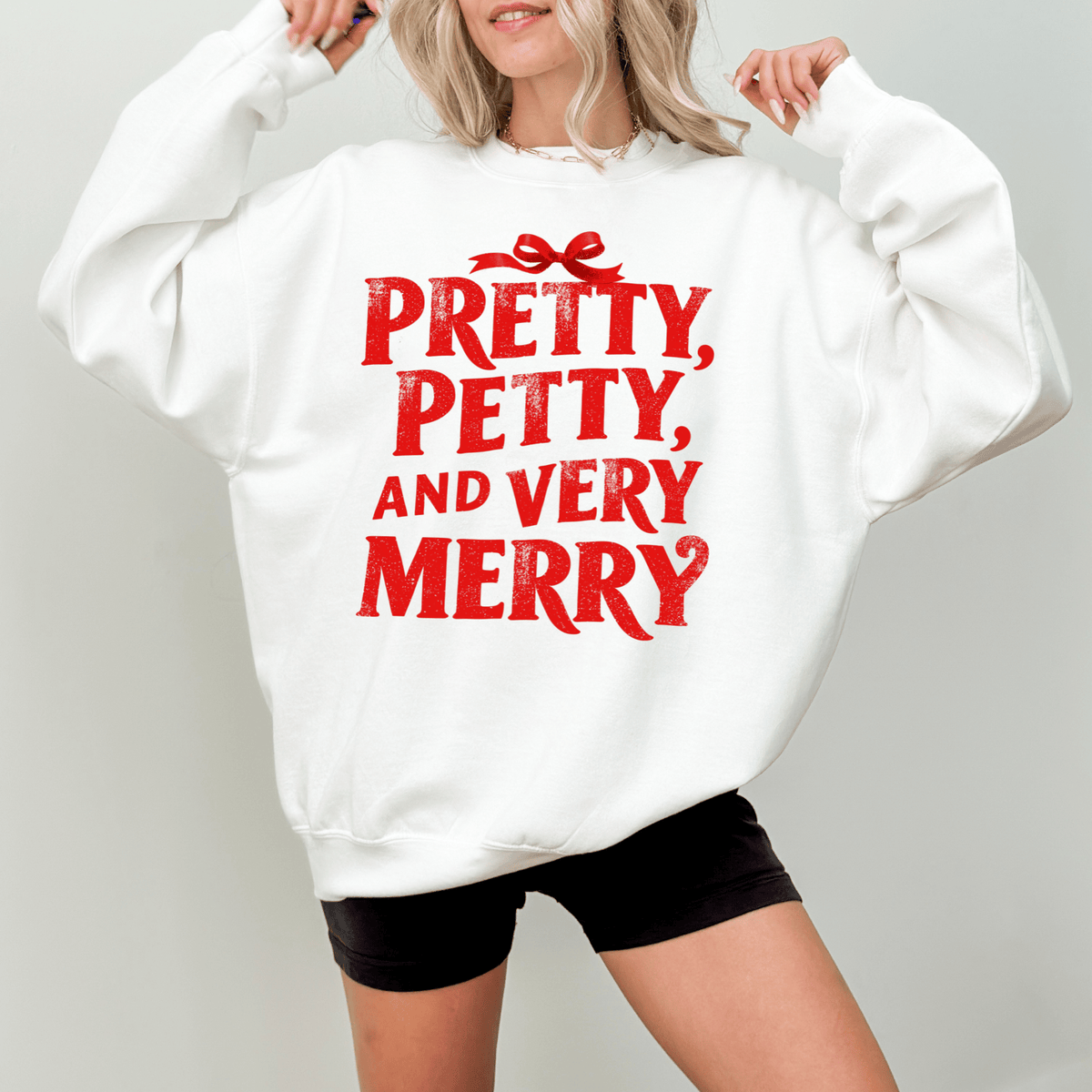 A woman wearing a white sweatshirt with the text "PRETTY, PETTY, AND VERY MERRY" printed on it.